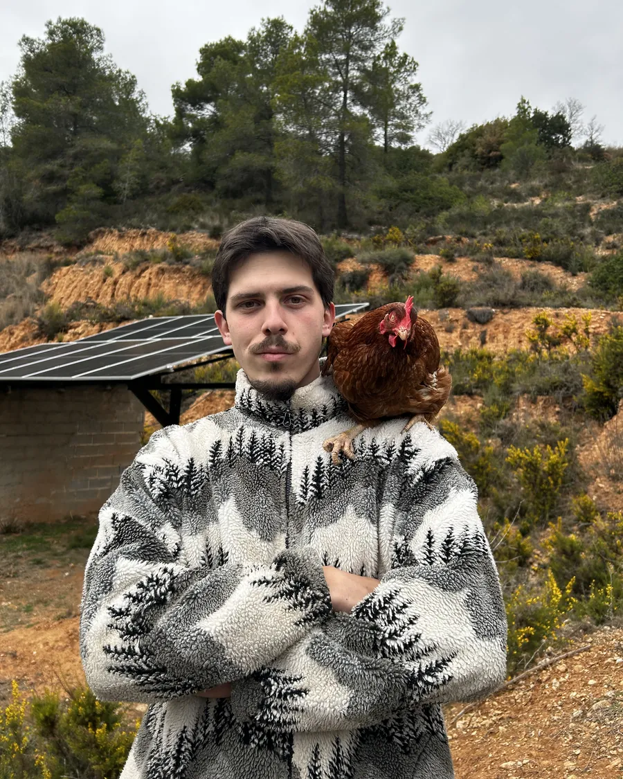 Iker en la finca con una gallina al hombro y las placas solares al fondo